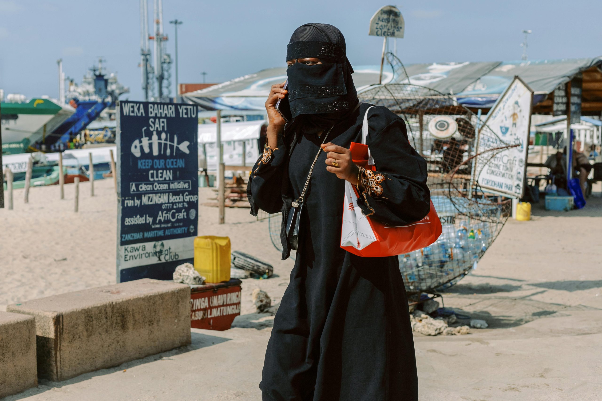 A woman in a black niqab walks by the beach in Zanzibar, showcasing local culture.